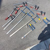 Full view of lot showing 10 wood clamps laid out on ground, 5 with red handles and 5 with yellow handles.