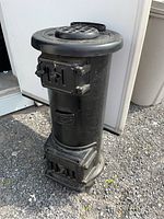 Front and left angled view of the black cylindrical cast iron stove showing footed base, upper and lower doors with latches, top circular vent, and embossed Acme logo.