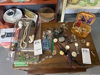 Overview of entire lot showing watches, costume jewelry including necklace, bracelets, brooches, locket, earrings, and pipe accessories arranged on wooden table.