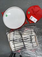 Top view of open red enamel paella pan and red lid of Dutch oven, with racks and dishes beneath