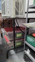 Photo showing metal framed folding table supporting an air conditioning unit and stacked plastic storage bins under it, highlighting the table's structure and height.