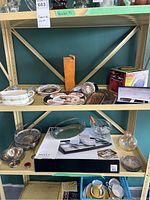 Two shelves showing assorted kitchenware, tableware, silverplate items, lighting, and boxed products.