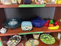 Front view of the shelf showing the camper candle holder, covered blue dish, glass fruit ornaments, and glass bowls