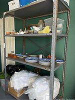 Full view of rusted metal shelving unit loaded with household items, showing frame condition and shelves