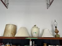 Wide shot of three lamps and four lamp shades on shelf, showing all items included in the lot.