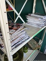 Shelves with stacks of home and decor magazines tightly packed on metal shelving unit, varying thicknesses and cover designs visible.