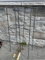 Full view of two black metal stands against stone wall showing 48 inch height and circular top rings