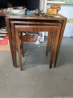 Three wooden nesting tables stacked together showing their shape and size.