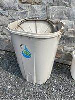 Front side view of beige rain barrel with water drop logo and repair on the top rim