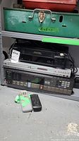 Stacked electronics showing Sony VHS player, Koss DVD player, and Sony stereo receiver with remotes in front.