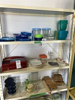 Shelves showing multiple plastic storage containers in blue and clear plastic with some lids, glass bowls, and decorative items including wooden serving trays and rolling pin