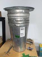 Stack of six galvanized metal maple syrup buckets with one lid placed on the top bucket.