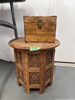 Carved wooden round table with intricate floral patterns shown with wooden box on top.