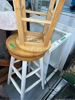 Larger wooden stool with natural wood round seat on top of white legs, showing wear on seat