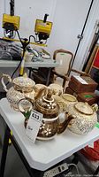 Full set of beige and gold tone teapots, cream jugs, and sugar bowls on white table