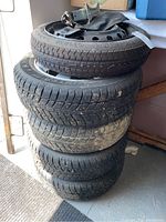 Stack of four used winter tires with one spare tire on top and a car jack on top of the spare tire, showing tread depth and overall appearance.