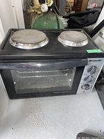 Front view of black Bravetti Platinum Pro toaster oven grill with two hot plates on top and control knobs on right side.