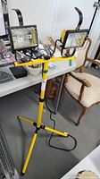 Yellow dual work lights mounted on an adjustable tripod stand, showing full height and structure.