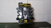 Sealed triple pack of PlayStation 2 controllers showing front of packaging with three controllers visible inside.