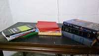 Overview of all books in the lot displayed on a table with worn edges and some stacked piles.