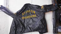 Back view of black leather jacket with yellow embroidered "RYERSON ENGINEERING" and "ER" patch on sleeve.