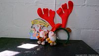 Clear photo of Christmas lot items on black surface showing three plush elves, reindeer antler headband, and Merry Christmas sign