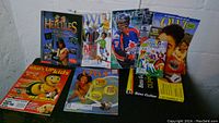 Photo of nine magazines and booklets including Hercules, What's UPkids with Bee Movie, Owl magazines, Sports Illustrated, comic book, bass guitar instruction booklet