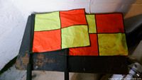 Two yellow and orange checkered nylon referee flags placed on a bench, showing some yellow discoloration.