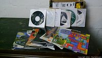 Photo showing multiple software CDs in paper sleeves arranged in a row above a set of video game booklets.