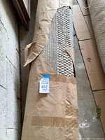 Photo showing the rolled-up 73 inch area rug partially covered with brown paper packaging, displaying the texture at the end of the roll.