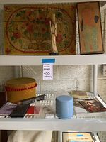 Lower shelf with decorative box, small cushions, wallet, blue multi-tiered container, and small art prints