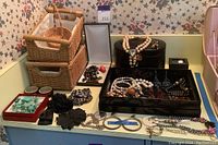 Overview of assorted jewelry with necklaces, earrings, hair ornaments, and jewelry boxes on a bathroom counter.