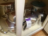 Cookware set in small kitchen cabinet, multiple stainless steel pots and pans with lids