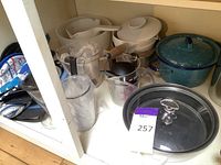 Photo showing assorted kitchen cookware including blue speckled roasting pan, cream ceramic pot with lid and wooden handle, measuring cups, and plastic pitcher.