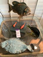 Photo showing a large mounted metal fish on a wooden base with two small orange fish and a flat metal fish sculpture on glass table