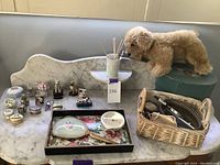 Wide shot of lot on marble surface including trinket boxes, vanity mirror, wicker basket with items, and plush dog toy on blue box