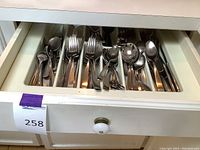 Opened drawer showing stainless steel flatware including knives, forks, and spoons organized in white plastic drawer organizer compartments.
