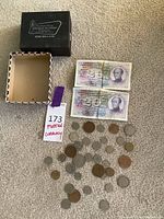 View of all coins spread on carpet alongside two foreign 20 Kroner bills and a black box for Anchor Robbins.