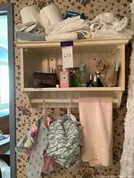 Wide shot of wooden shelf with multiple towels stacked on top and various fragrance bottles arranged inside, cloth pouches hanging below.