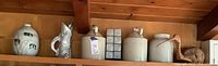 Shelf with four stoneware moonshine jugs, pewter fish pitcher, wooden duck, white ceramic vase, and decorative votive holder