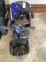 Front view of blue Pride mobility scooter showing front basket, padded seat, extra rear basket and charging cord.