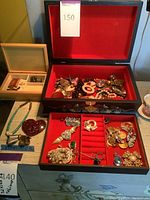 Jewelry boxes containing assorted costume jewelry including large brooches and earrings, visible pieces with rhinestones, faux pearls, and colorful stones.