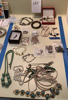 Overview of assorted jewelry including rings, bracelets, necklaces, earrings and charms laid out on table under lot number