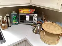 Wide view of countertop showing toaster oven, Palmolive dish detergent, Glad cling wrap, stainless steel insulated bottle, wooden turntables, Alessi tea kettle