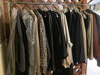 Full wardrobe rack loaded with various hanging women's clothing predominantly in neutral, beige, brown, black colors, visible patterns and textures, multiple jackets and tops.