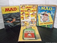 Four Mad Magazine issues sealed in plastic and backed by boards, showing cover artwork with colorful satirical illustrations.