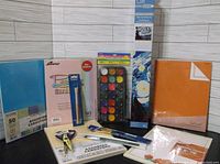 Front view of the entire lot showing assorted cardstock packs, watercolor paint set, multiple paint brushes, a paint palette knife, and art paper pads.