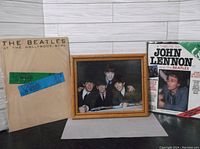 Framed color photo of The Beatles with booklet and magazine near each other on a white wood background.