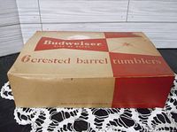Closed original cardboard box labeled 'Budweiser 6 crested barrel tumblers' with some wear and discoloration to box.