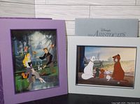 Photo showing Sleeping Beauty lithograph with purple mat and Aristocats lithograph with gray mat and folder